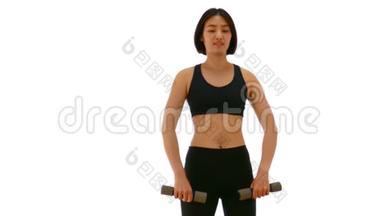 漂亮的泰国亚裔女运动员举起哑铃在两只手臂站立抬高或V举姿势。 举重锻炼有氧运动